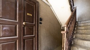 Une porte en bois avec une poignée en laiton et une plaque nominative, un escalier en pierre avec une rampe en bois, et un mur à la texture particulière.