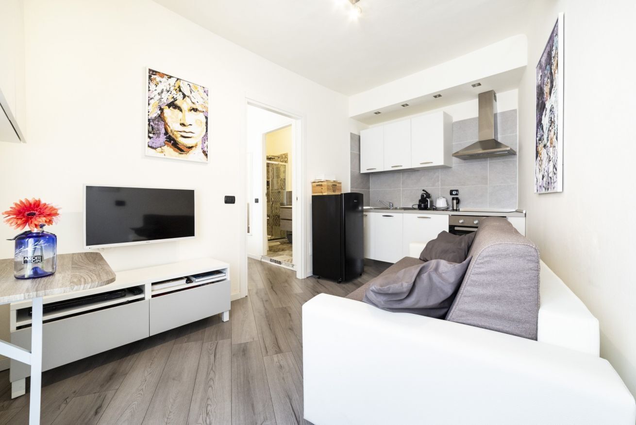 Un soggiorno moderno con televisione a schermo piatto, un divano bianco e un'area pranzo con cucina sullo sfondo.
