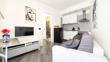 Un soggiorno moderno con televisione a schermo piatto, un divano bianco e un'area pranzo con cucina sullo sfondo.