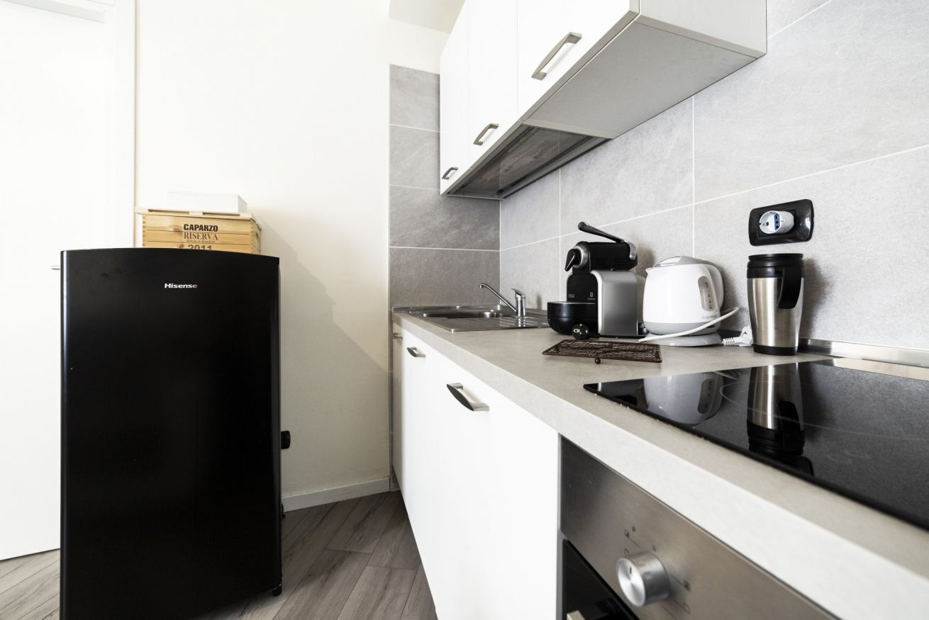 Una cucina moderna con frigorifero nero, mobili bianchi, piano cottura in acciaio inossidabile e macchina da caffè.