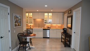 Cocina compacta con armarios blancos, lavavajillas y comedor con mesa y sillas.