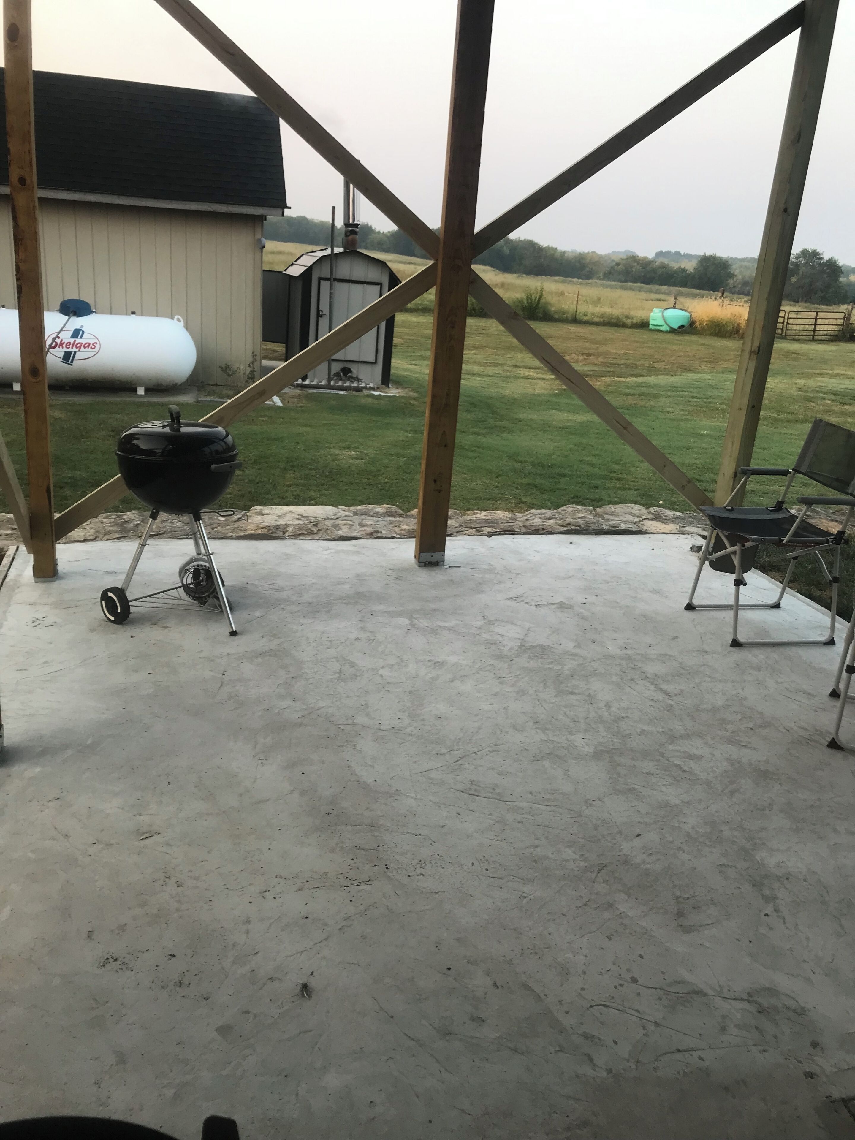 Een overdekt terras met een betonnen vloer, een zwarte barbecue en een stoel.
