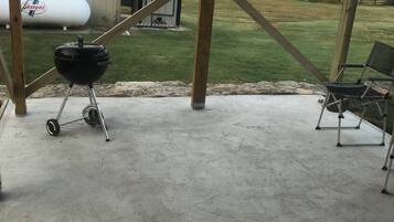 Een overdekt terras met een betonnen vloer, een zwarte barbecue en een stoel.