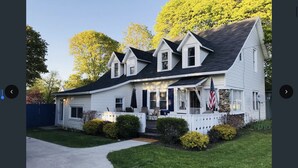 A two-story house with a front porch, a stone foundation, and a flag.