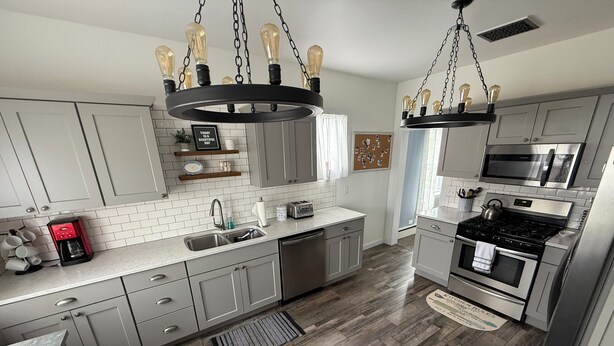A modern kitchen with grey cabinets, a stainless steel range, a built-in oven, a microwave, and a coffee maker.