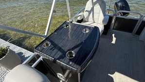 A boat deck with seating, a table, and a clear view of the water and distant shoreline.