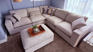 A living room with a sectional sofa, a coffee table, and a window with curtains.