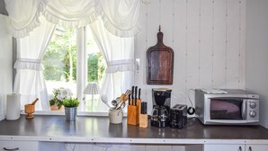 Une cuisine avec des meubles blancs, une fenêtre avec des rideaux blancs, une machine à café, un grille-pain et un four à micro-ondes.