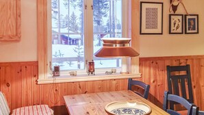 A wooden interior with a dining table, chairs, a window with a view of snow-covered trees, and framed artwork on the wall. - 3 bedroom stunning home in Särna (Särna)