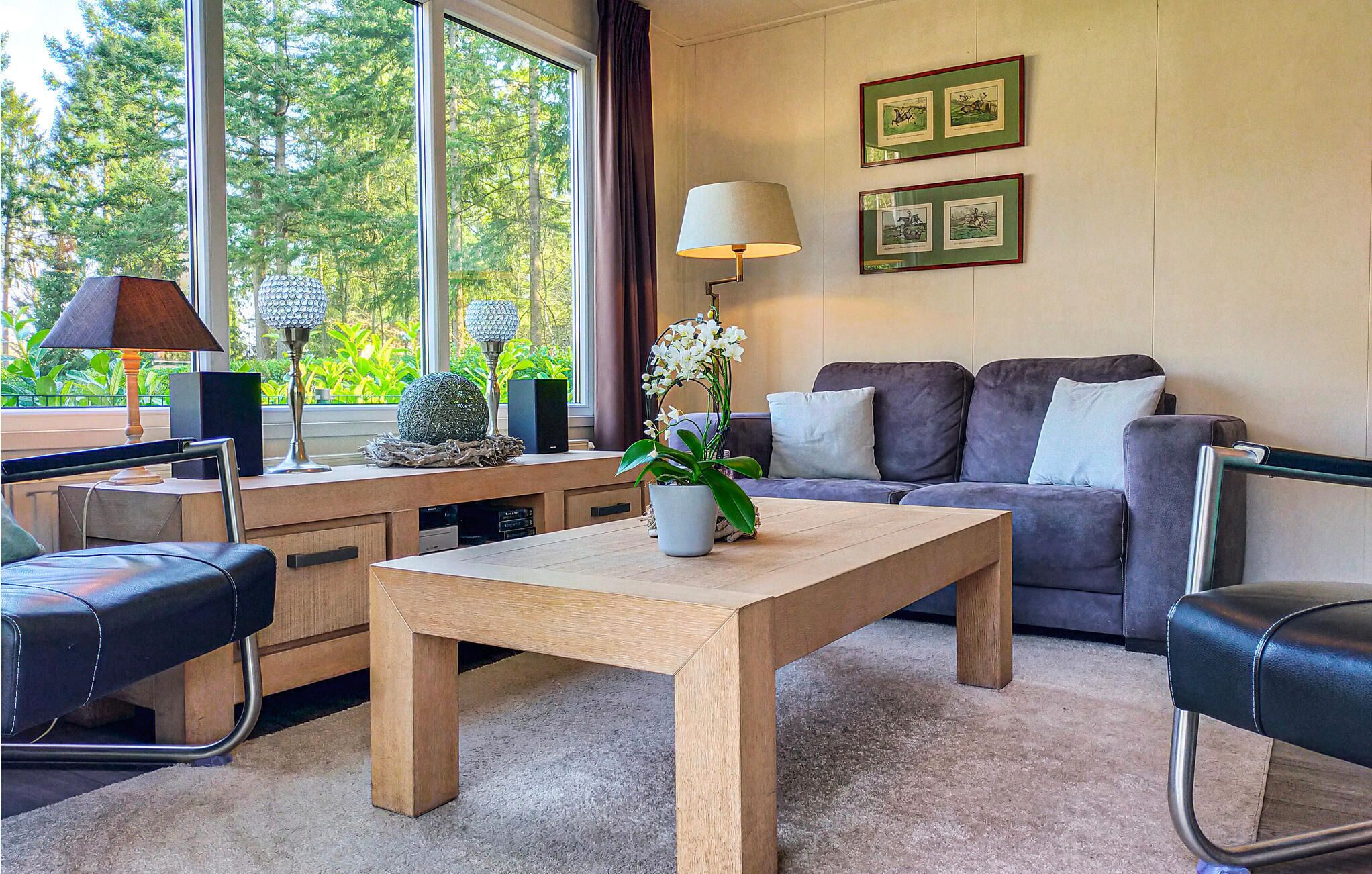 A modern living room with a wooden coffee table, a grey sofa, and a desk with a lamp and decorative items.