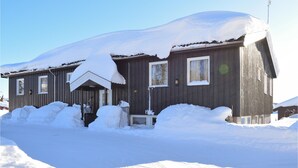 Una cabaña de madera con techo nevado y un pequeño porche.
