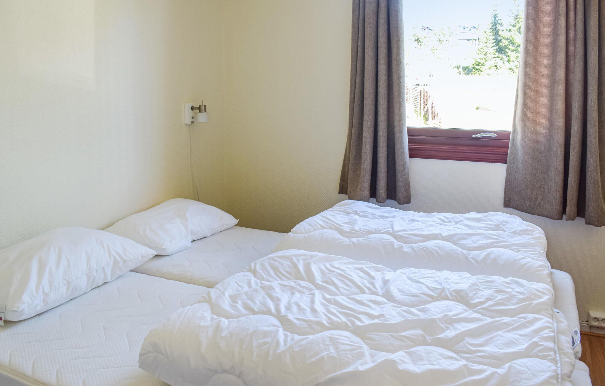 A hotel room with two beds, white bedding, a window with curtains, and a view of greenery outside.