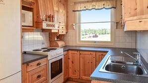 Cocina compacta con armarios de madera, microondas integrado, estufa y ventana con vistas a un bosque.