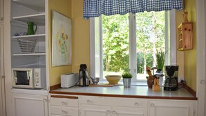 Una cocina con gabinetes blancos, microondas, tostadora, cafetera y una ventana con vista a árboles.
