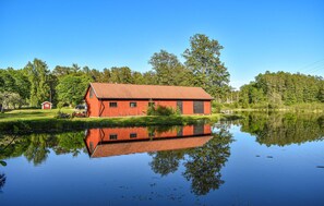 Un edificio rojo de madera con techo inclinado, ubicado junto a un lago tranquilo con reflejos claros.