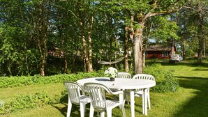 Un conjunto de comedor exterior blanco con sillas y una mesa, rodeado de exuberante vegetación y árboles.