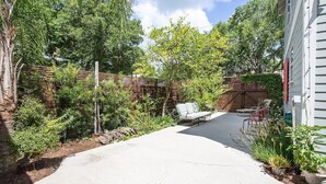 A backyard with a concrete patio, a white outdoor chair, a red chair, and various plants. - Luxurious indoor/outdoor Family Paradise in downtown St Augustine (St. Augustine)