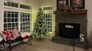 A cozy living room with a fireplace, a Christmas tree, and a bench with festive pillows. - Where the Missouri sky wakes up first.  Peaceful mornings you’ll never forget. (Warrensburg)