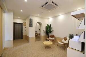 A reception area with a reception desk, a seating area with two chairs, a large potted plant, and a door leading to another room.