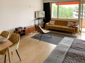 Ein modernes Wohnzimmer mit einer Couch, einem Esstisch mit Stühlen, einem Fernseher und einem Fenster mit Blick auf Gebäude.