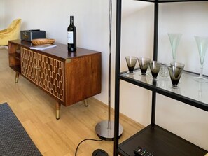 Ein modernes Wohnzimmer mit einem Holzschrank, einer Stehlampe und einem Glastischchen mit dekorativen Vasen.