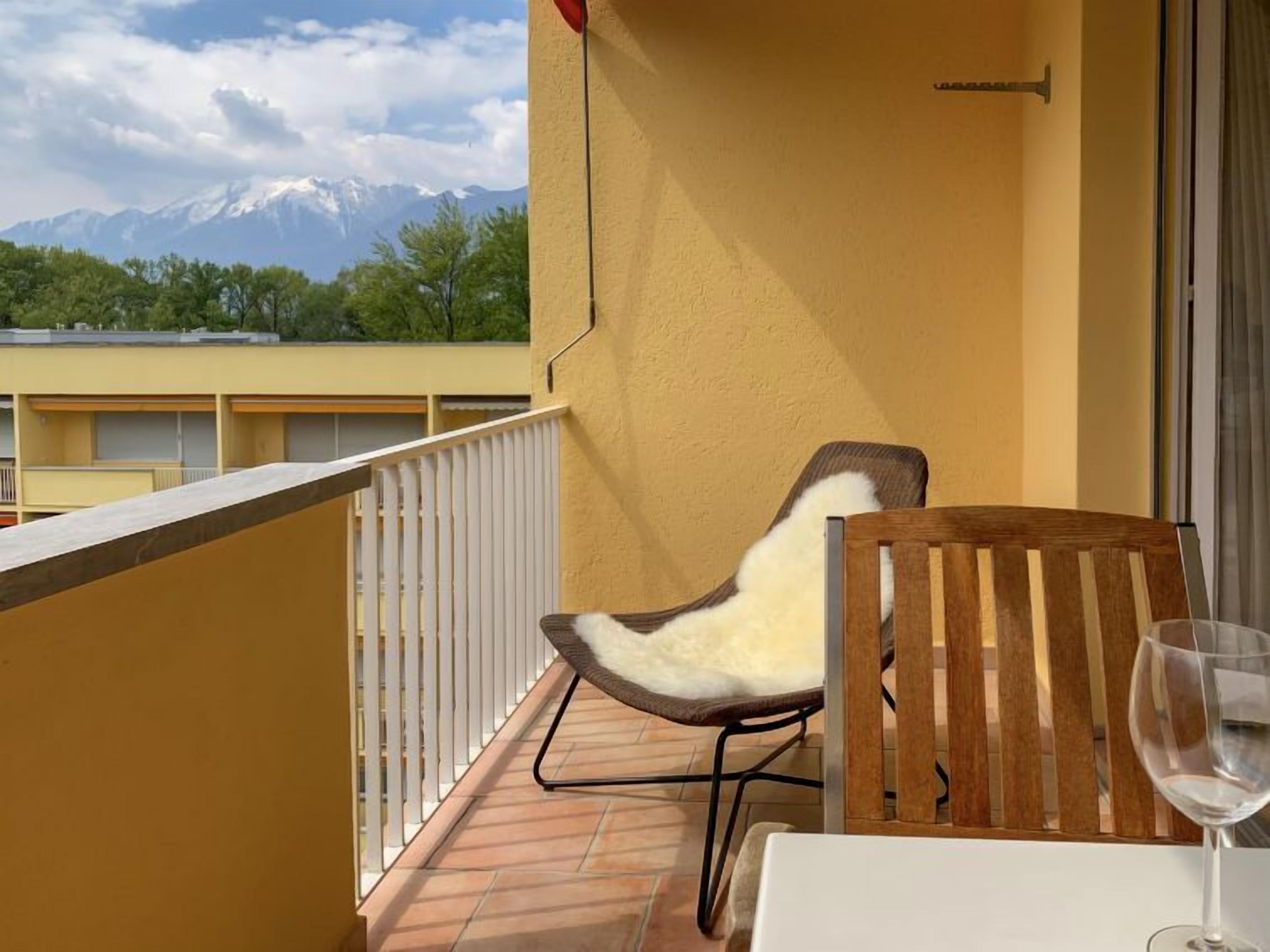 A balcony with a chair and a table, a glass of wine, and a mountain view.