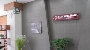A reception area with a luggage sign, a clock, a framed picture, and a sign for Stay Well Hotel. - Staywell Hotel (Busan)