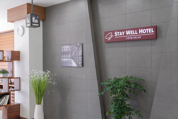 A reception area with a luggage sign, a clock, a framed picture, and a sign for Stay Well Hotel. - Staywell Hotel (Busan)