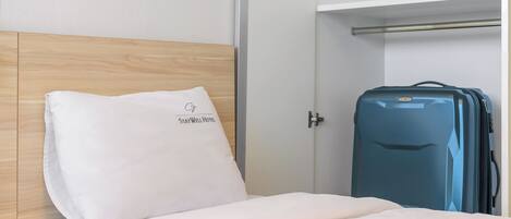 A hotel room with a bed, a white pillow with a logo, a blue suitcase, and a wardrobe.