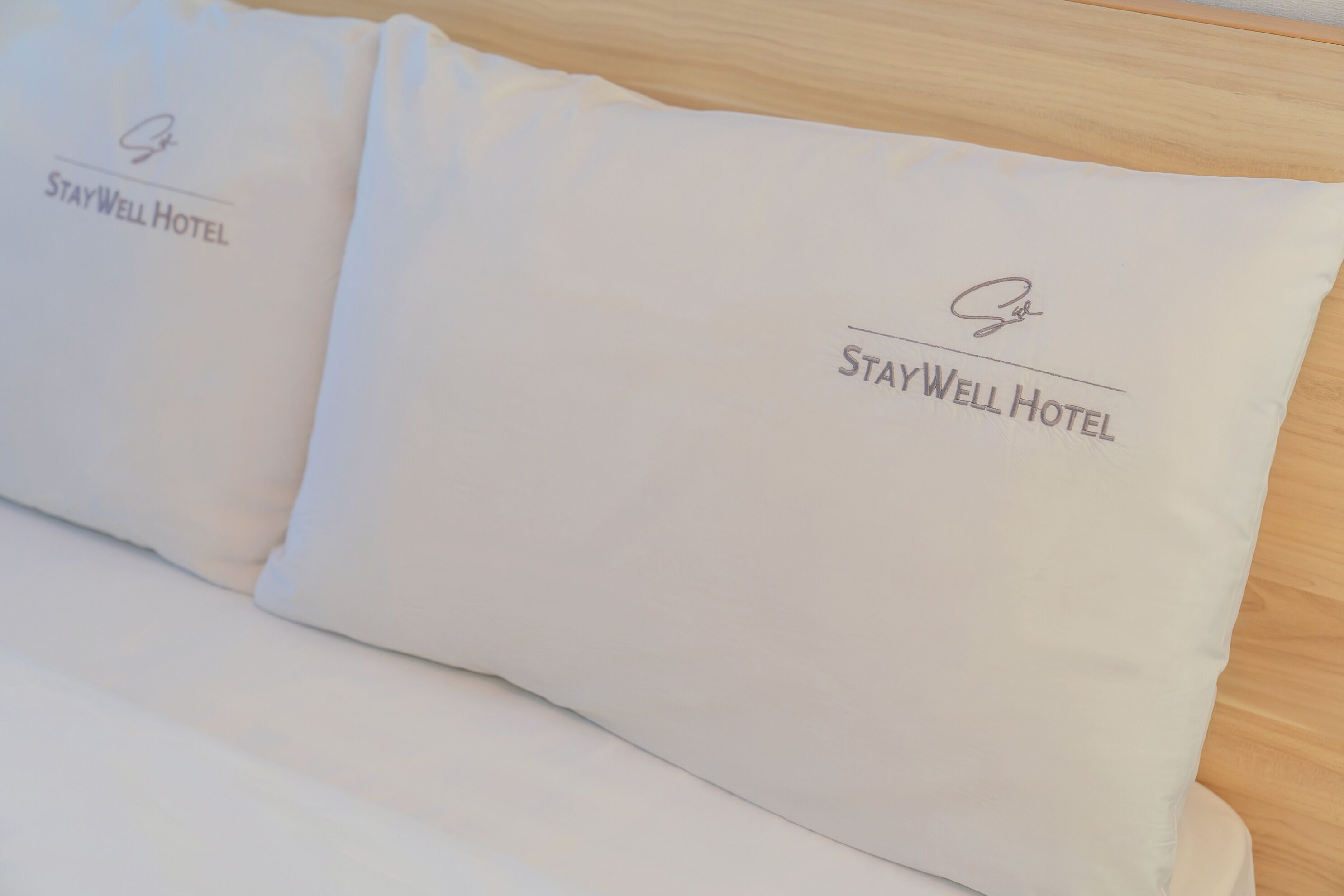 Dos almohadas con el logotipo del Hotel StayWell sobre una superficie de madera.
