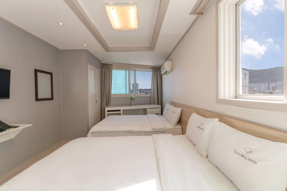 Habitación de hotel con dos camas, un escritorio, un televisor y una ventana con vistas a la ciudad.