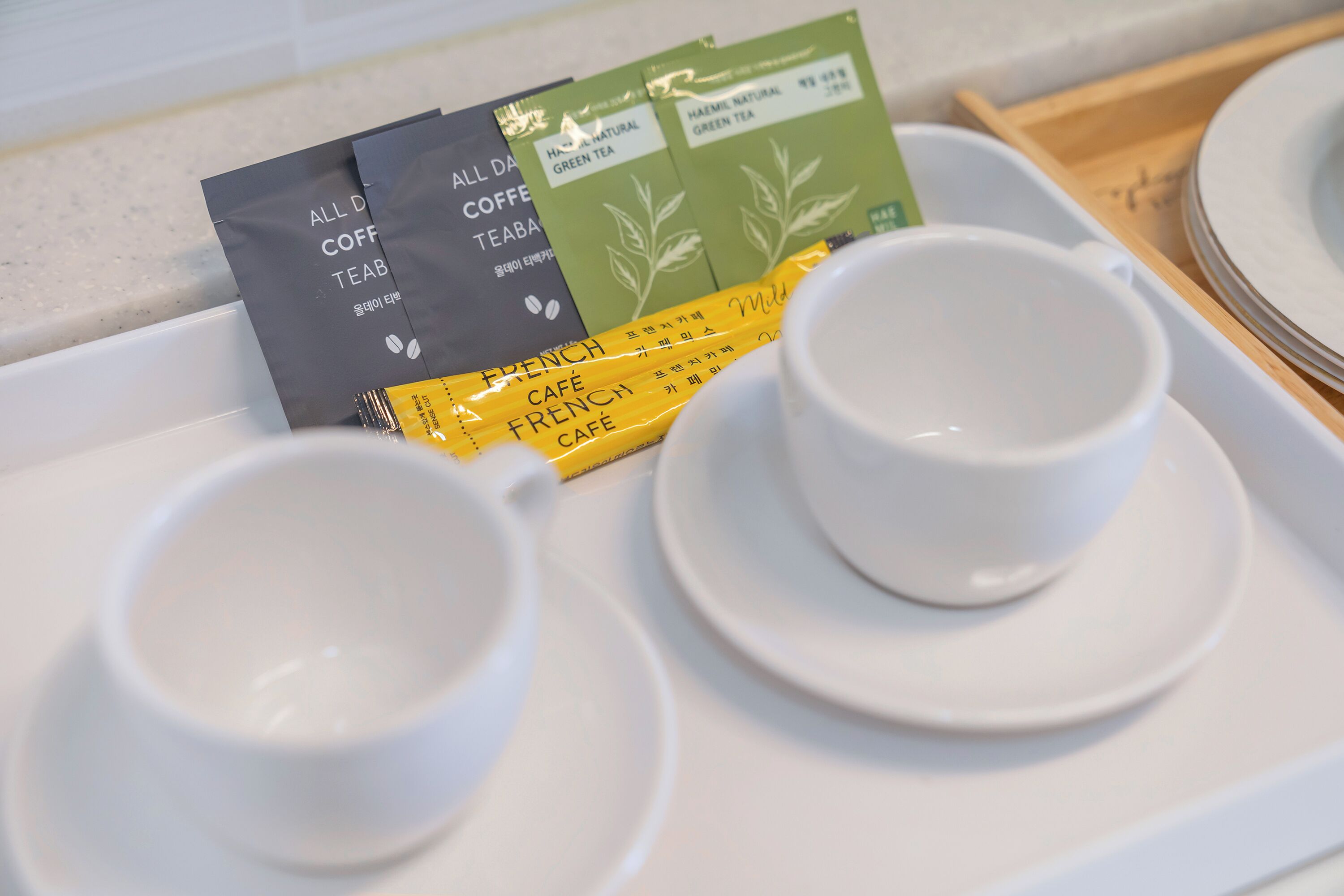 A tray with two white cups and a tea bag labeled "ALL DAY COFFEE TEABO" and "HAEM NATURAL GREEN TEA".