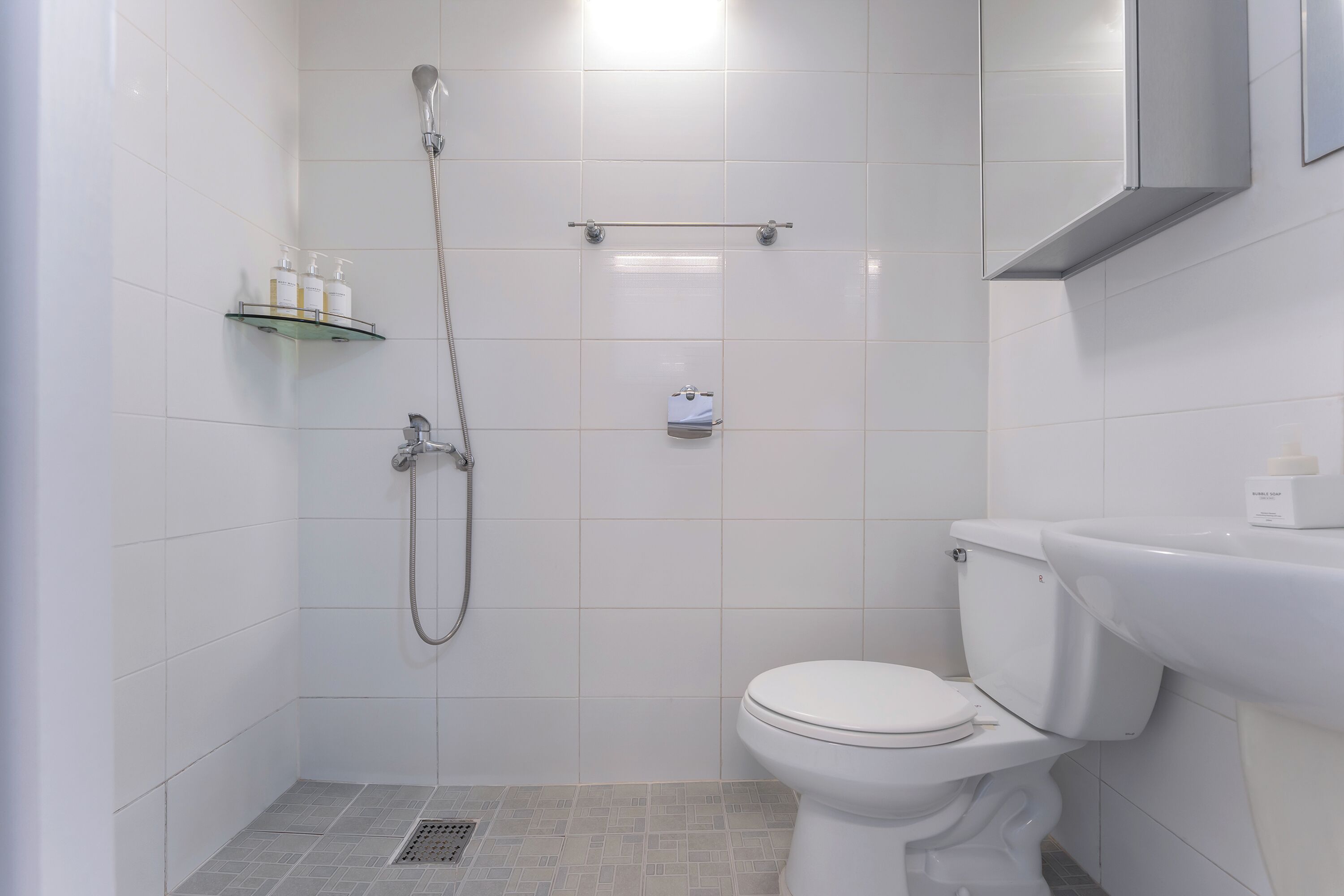 Un baño moderno con ducha, inodoro y un estante con artículos de aseo.
