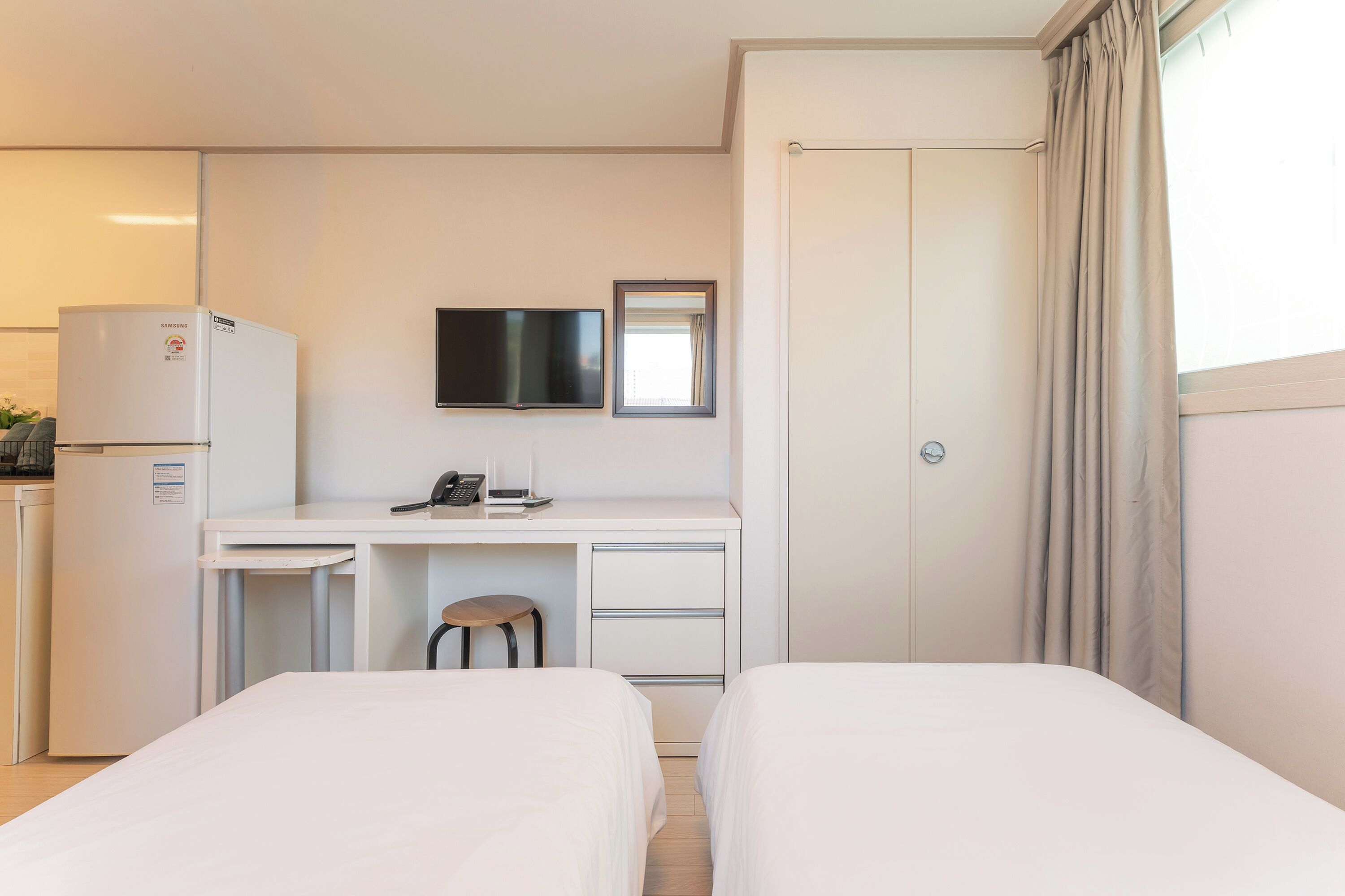 Ein Hotelzimmer mit zwei Betten, einem Schreibtisch mit Stuhl, einem Fernseher und einer Minibar.