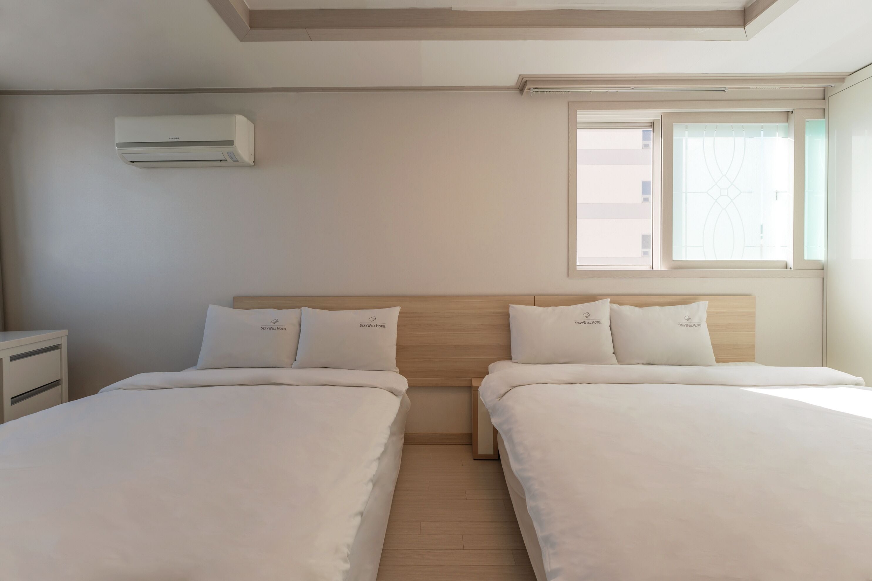 Ein Hotelzimmer mit zwei Betten, einem Holz-Kopfteil, einem Nachttisch und einer Klimaanlage.