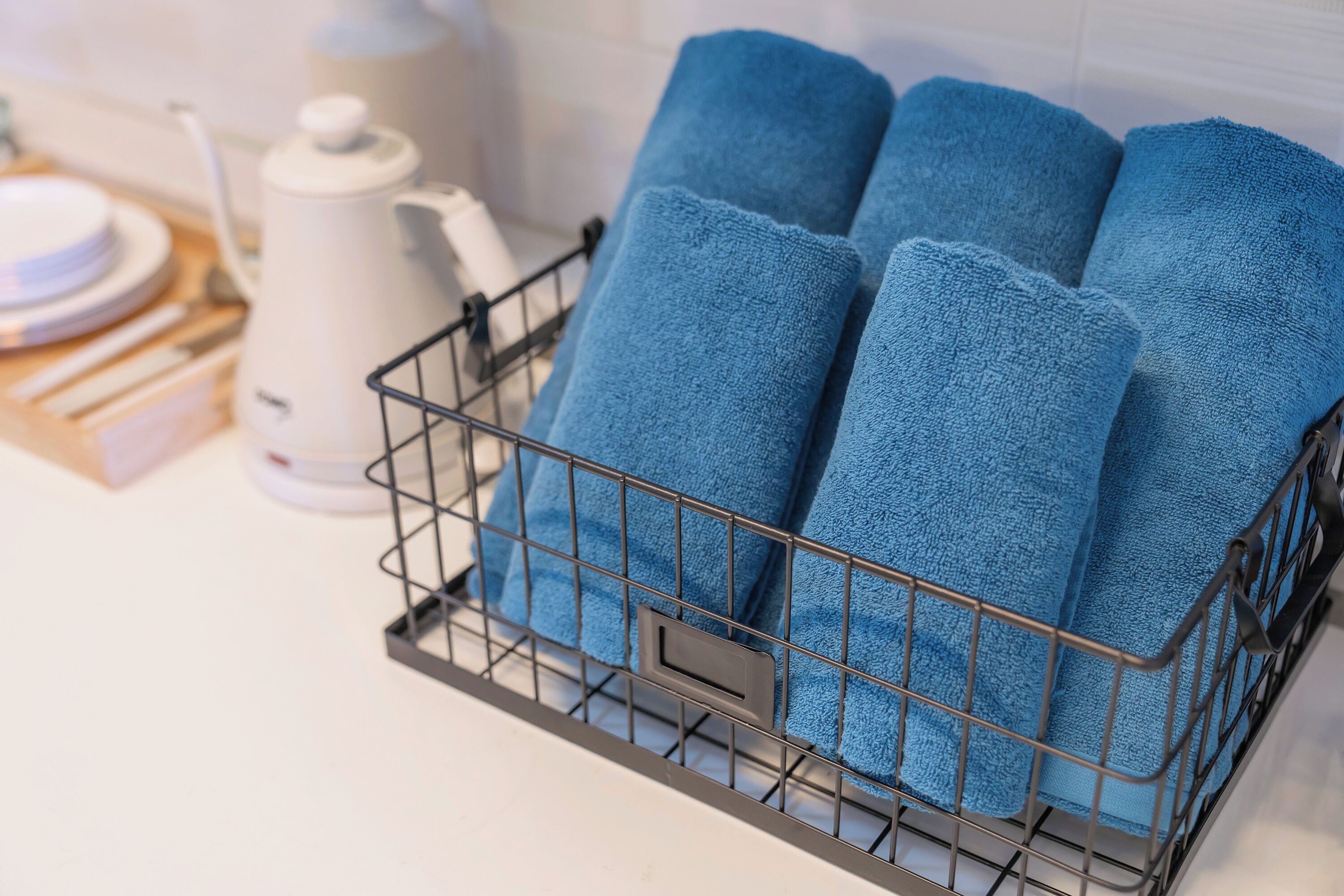 Una cesta de metal con cuatro toallas azules sobre una encimera de cocina.