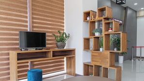 A modern hotel lobby with a wooden reception desk, a flat-screen TV, a blue ottoman, and a wooden plant display. - Staywell Hotel (Busan)