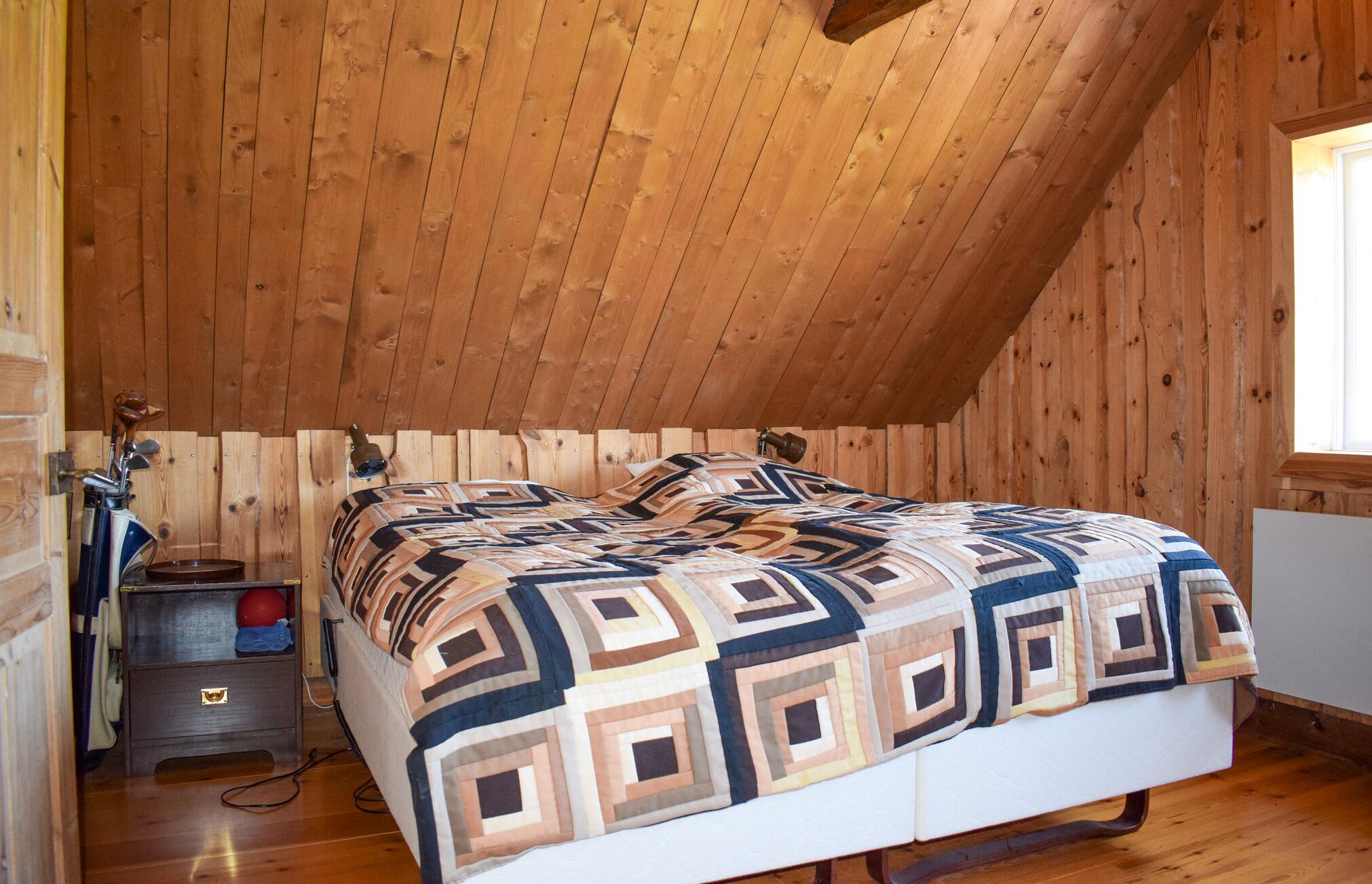Ein Schlafzimmer im Dachgeschoss mit Holzwandverkleidung, einem Bett, einem Nachttisch und einem Fenster.