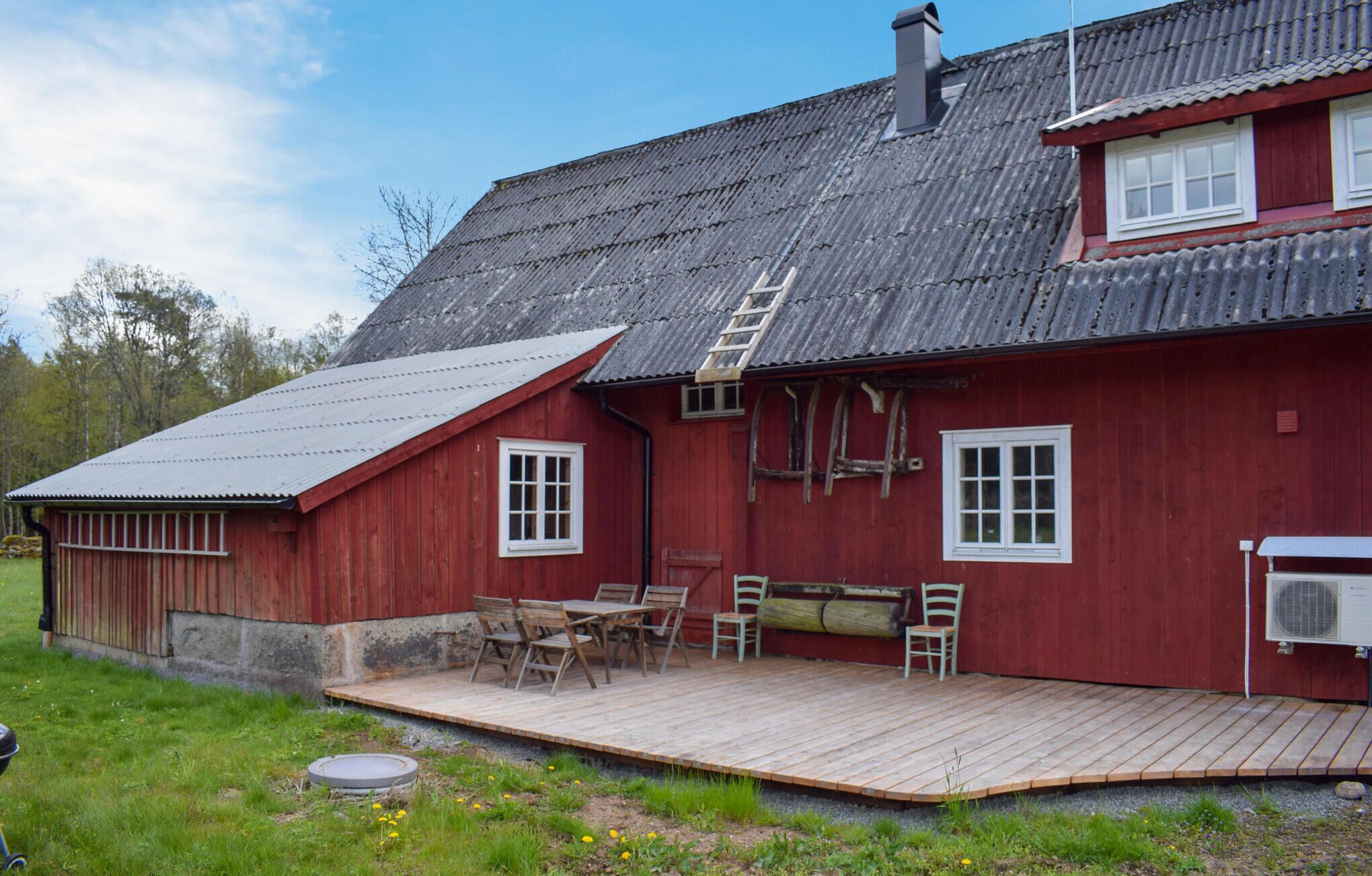 Ein rotes Holzhaus mit einem Metalldach, einer Holzdiele und einer kleinen Außenbereich-Sitzgelegenheit mit Stühlen und einem Tisch.