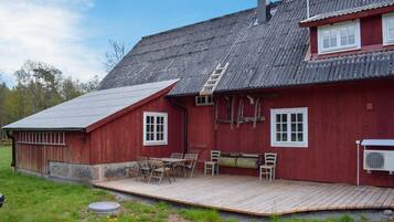 Ein rotes Holzhaus mit einem Metalldach, einer Holzdiele und einer kleinen Außenbereich-Sitzgelegenheit mit Stühlen und einem Tisch.
