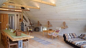Une pièce mansardée chaleureuse, avec une table à manger en bois, des chaises, un canapé et un décor rustique comprenant un poêle à bois, des tonneaux et un cheval à bascule.
