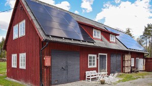 Une grange rouge avec des panneaux solaires sur le toit, une porte de garage noire et un banc à l’extérieur.