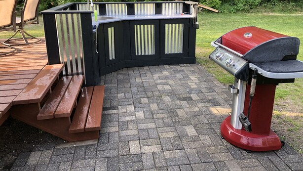 Un espacio para parrilladas con una parrilla, bancos de madera y un patio empedrado.