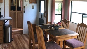 Una cocina compacta para vehículo recreativo, con armarios de madera, una mesa de comedor con sillas y una ventana con cortinas.