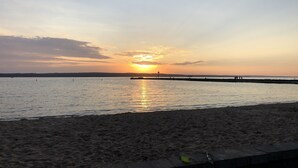 Una playa con un atardecer sobre el agua, un muelle y algunas personas a lo lejos.