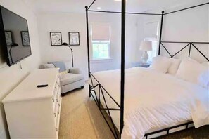 A bedroom with a four-poster bed, a dresser, a television, and framed artwork on the wall.