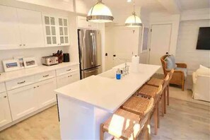 A modern kitchen with white cabinetry, a large island, and a stainless steel refrigerator.