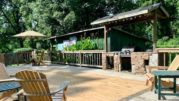 En udendørs terrasse med træterrasse, Adirondack-stole, grill og en overdækket siddeplads.