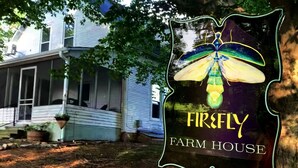 Et hus med en veranda og et skilt, der står 'Firefly Farm House'.
