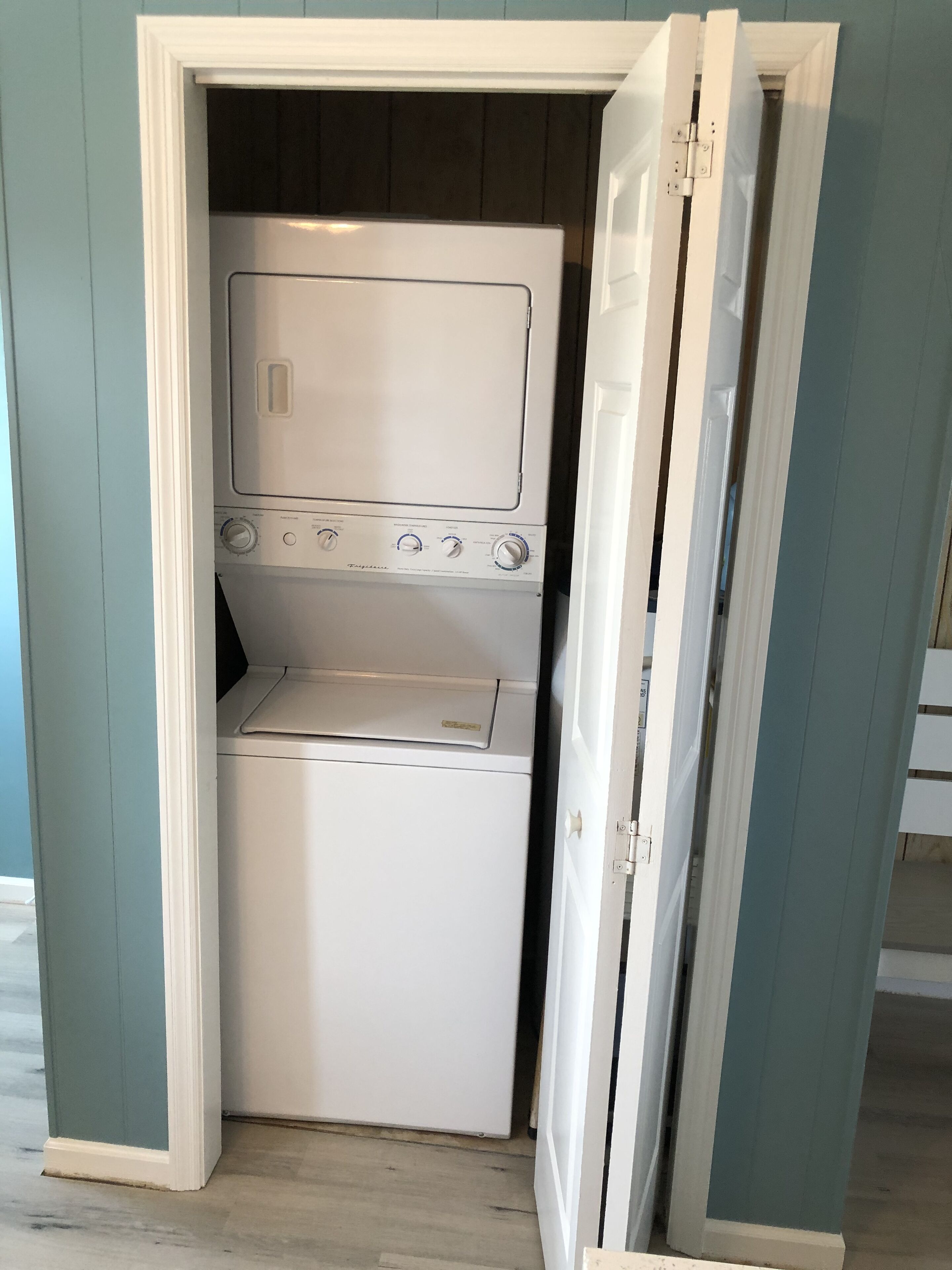 A compact laundry room with a built-in washer and dryer, enclosed by a door with a white frame.
